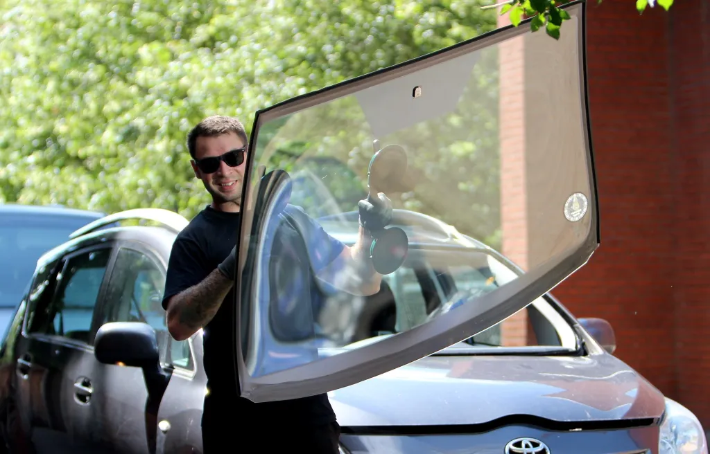 Technician carefully positioning a new windscreen onto a vehicle frame using suction cups